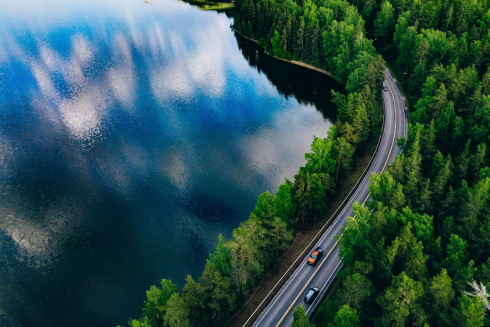 Cards driving down a curving road alongside a lake and forest area.
